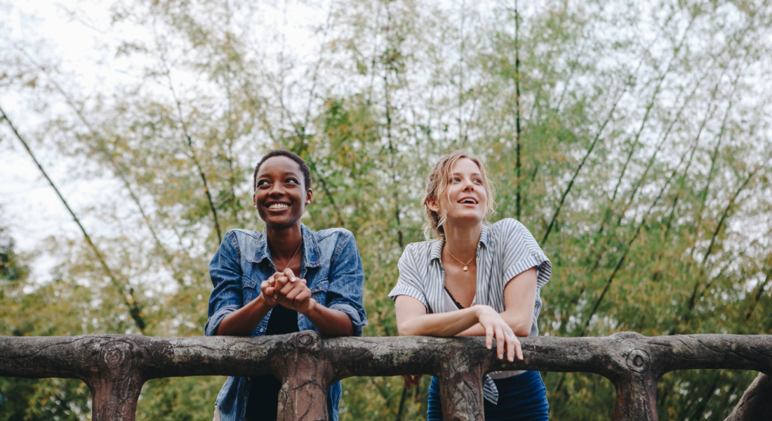 two women leaning on a bridge railing